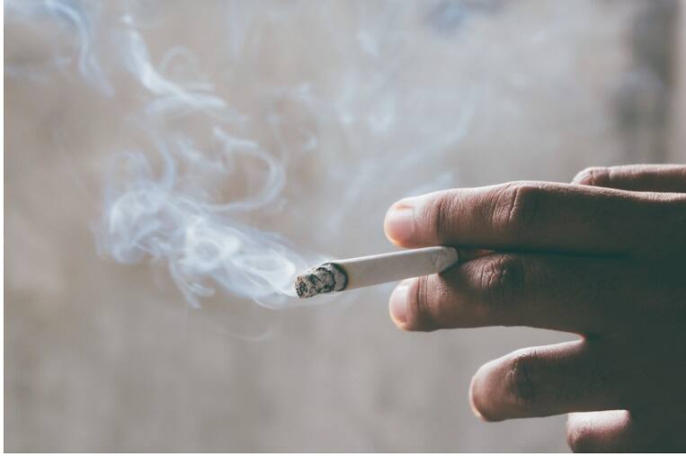 Close-up of a hand holding a lit cigarette with smoke swirling, representing nicotine addiction and substance abuse issues