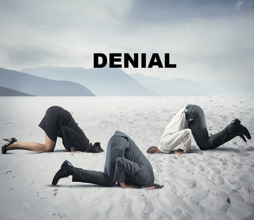 Conceptual image depicting denial in functioning alcoholics: three people with heads buried in sand on a beach, with 'DENIAL' text overhead