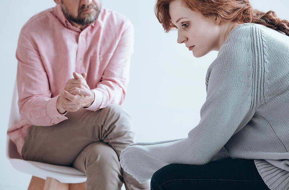 A concerned woman sitting with her head down during a counseling session, while a man in a pink shirt listens attentively, emphasizing the importance of emotional support in overcoming alcoholism.